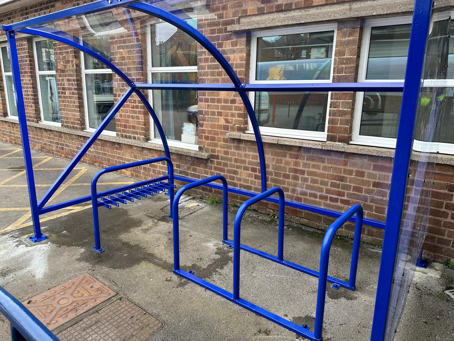 Powder coated blue curved school bike shelter with clear plastic cladding, including powder coated scooter rack and Sheffield hoops for secure cycle and scooter storage.